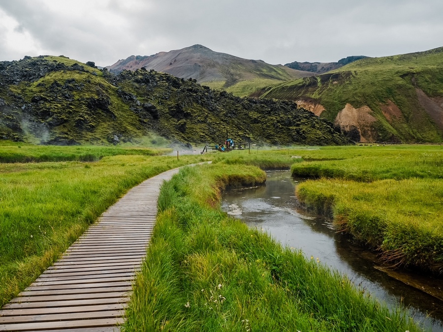 在冰岛的Landmannalaugar露营地，一群游客在热浴中放松，通往天然温泉的木路
